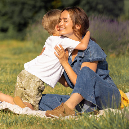 A child hugging a woman in a denim outfit and brown sneakers.